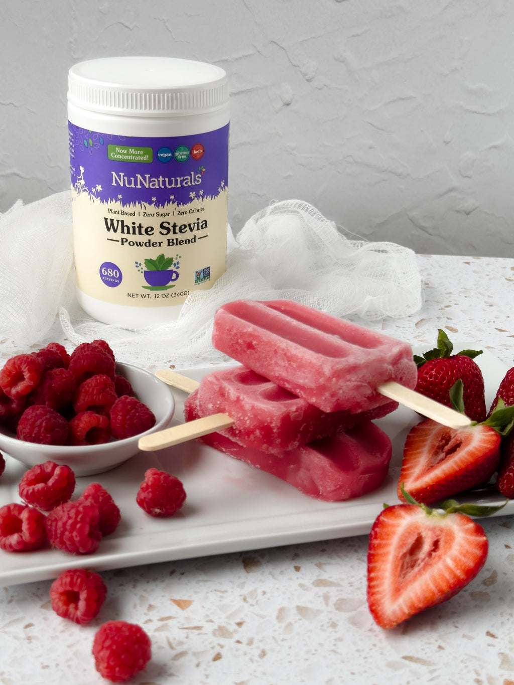 White Stevia Powder tub behind stacked pink fruit popsicles on a tray, with raspberries and strawberries around