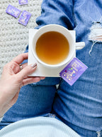White Stevia Powder Blend Packets tea bag style packet resting on a saucer beside a cup of tea, held over jeans
