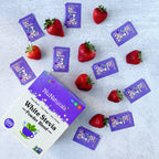 White Stevia Powder Blend Packets box with loose purple packets scattered among strawberries on a gray surface
