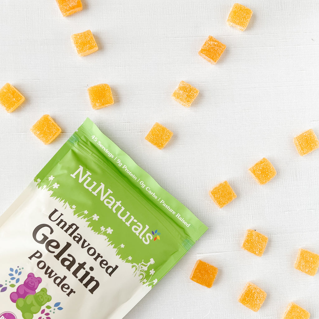 Unflavored Gelatin pouch in the corner of the frame with orange gummy squares scattered on a white surface