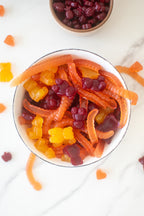 Bowl of orange, yellow, and purple gummy bears and gummy worms on marble, viewed from above