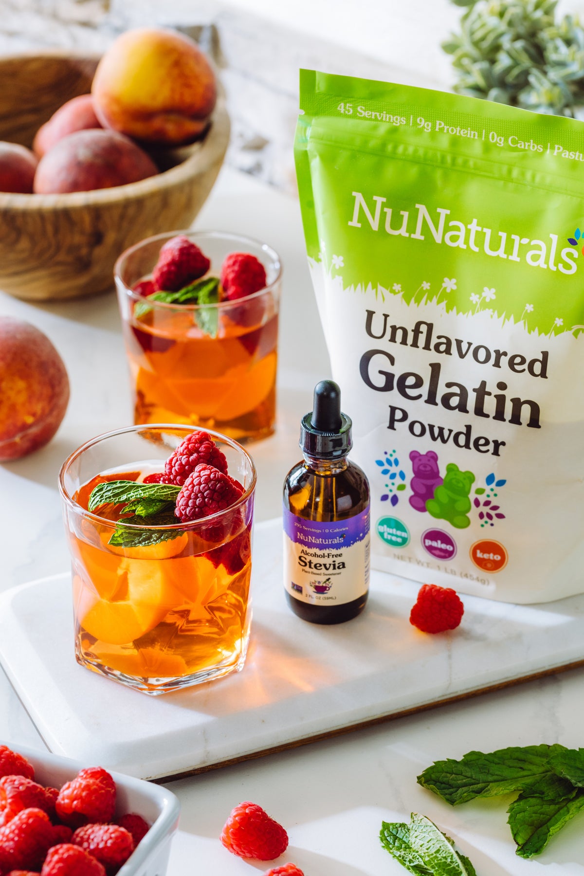 Unflavored Gelatin pouch and a stevia dropper bottle beside drinks with raspberries, mint and peach slices