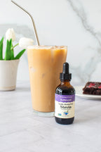 Vanilla Alcohol-Free Stevia 2 oz dropper bottle in front of an iced latte, with a brownie slice behind