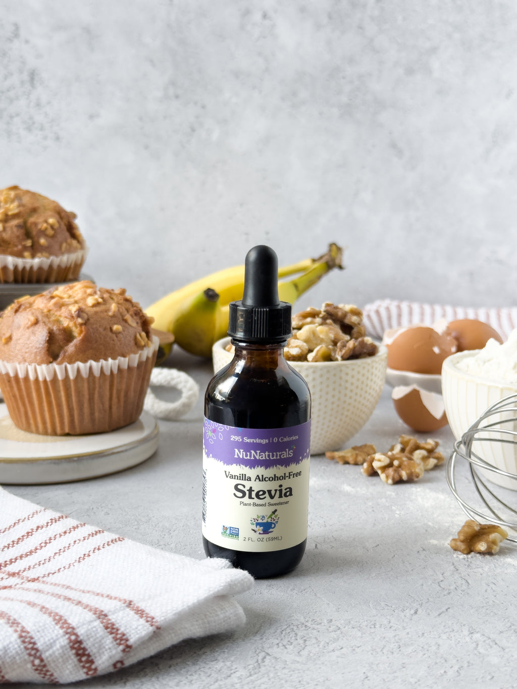 Vanilla Alcohol-Free Stevia 2 oz dropper bottle on a counter with muffins, bananas, walnuts, eggs and a whisk