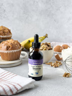 Vanilla Alcohol-Free Stevia 2 oz dropper bottle on a counter with muffins, bananas, walnuts, eggs and a whisk