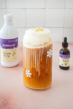 Vanilla Alcohol-Free Stevia 2 oz dropper bottle at right of a tall glass of iced coffee with cream, next to a syrup bottle